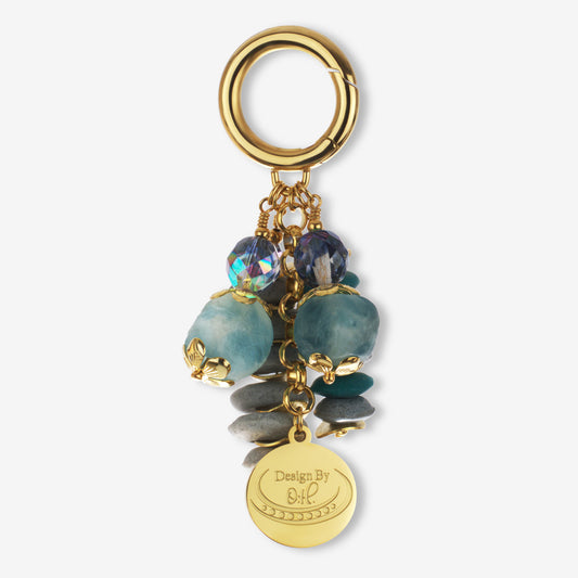 Ayisibea Bag Charm featuring blue-gray, gray, and aqua Ghanaian recycled glass beads with gold-plated wavy discs and crystal accents.
