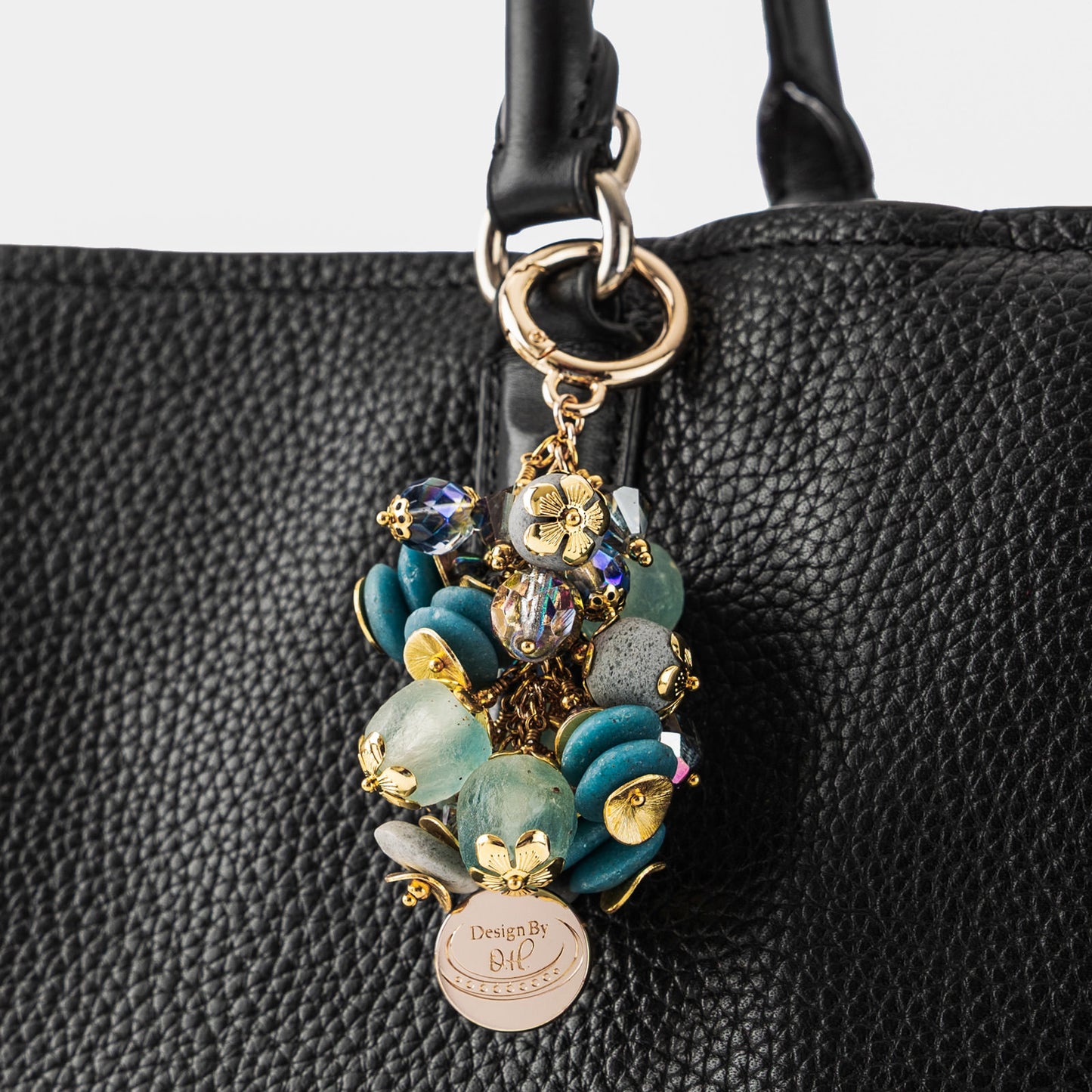 Close-up of Ayisibea charm showing textured blue-gray beads, aqua crystals, and gold-plated disc elements.