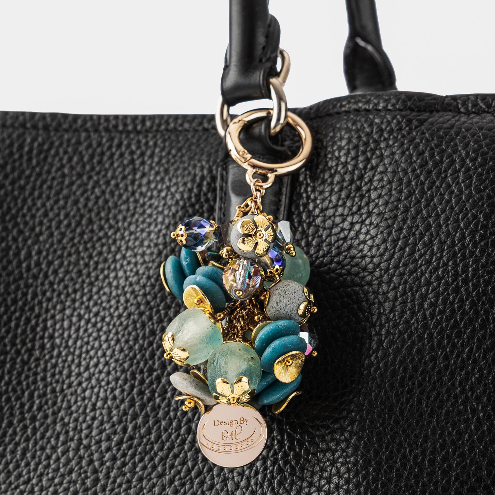 Close-up of Ayisibea charm showing textured blue-gray beads, aqua crystals, and gold-plated disc elements.