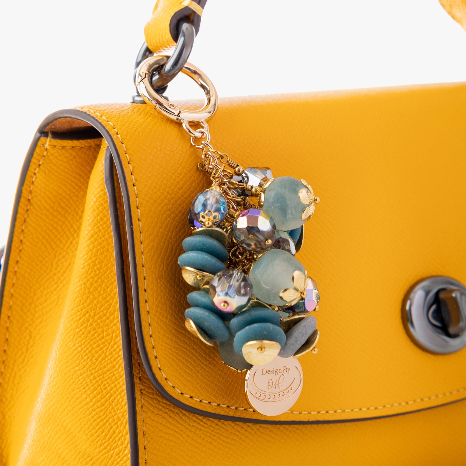 Ayisibea Bag Charm clipped to a handbag, showcasing its calming blue-gray and aqua palette symbolizing healthy personal boundaries.