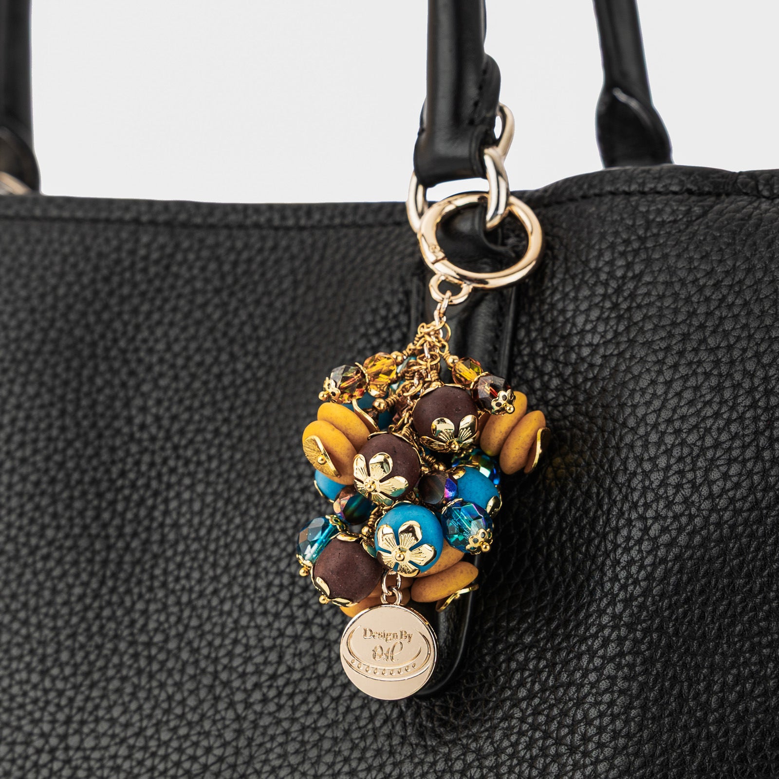 Odamea Bag Charm attached to a handbag, highlighting its brown, yellow, and aqua color palette symbolizing discipline and determination.