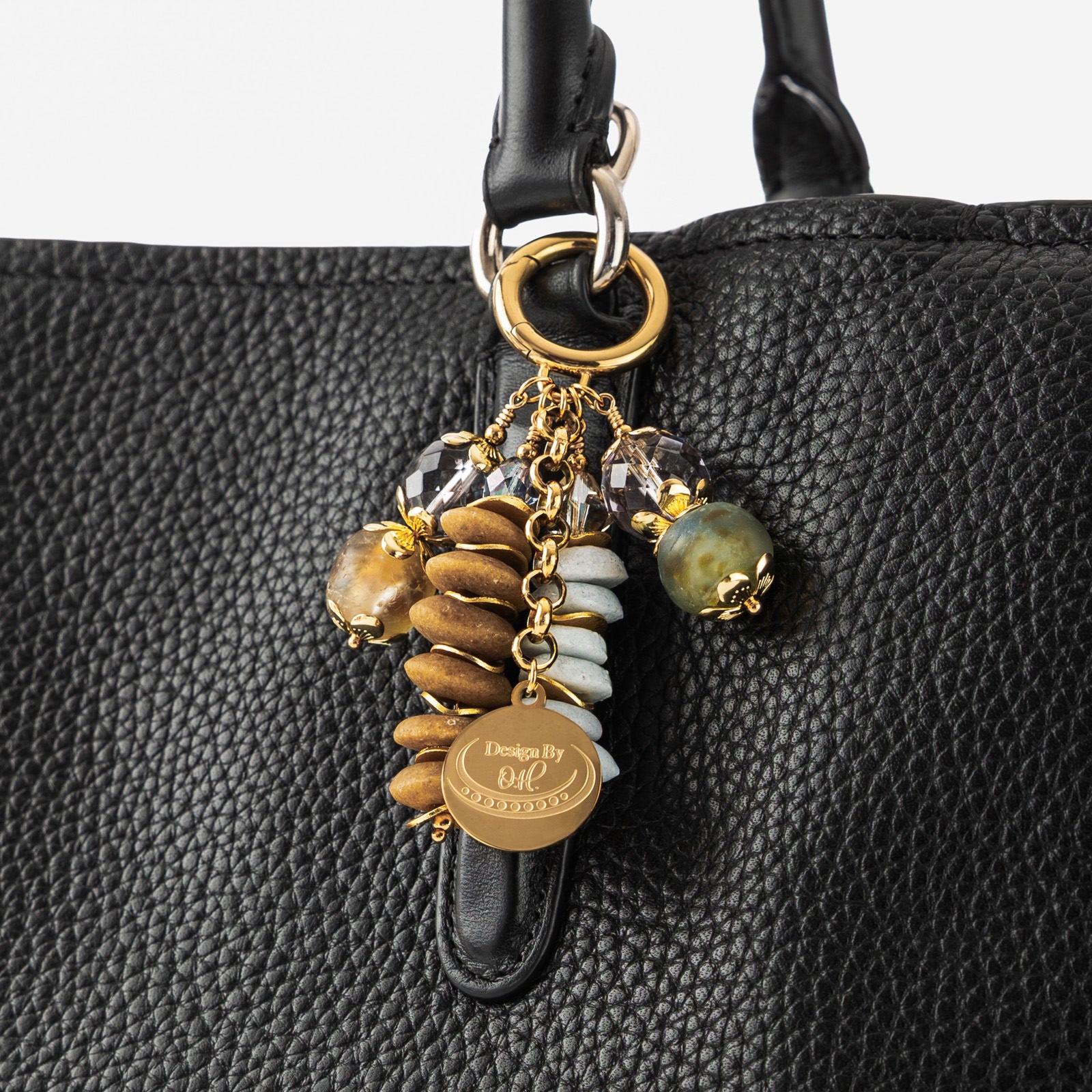 Osaebea Bag Charm clipped to a handbag, showcasing its light blue and brown color palette symbolizing contentment and grounded joy.