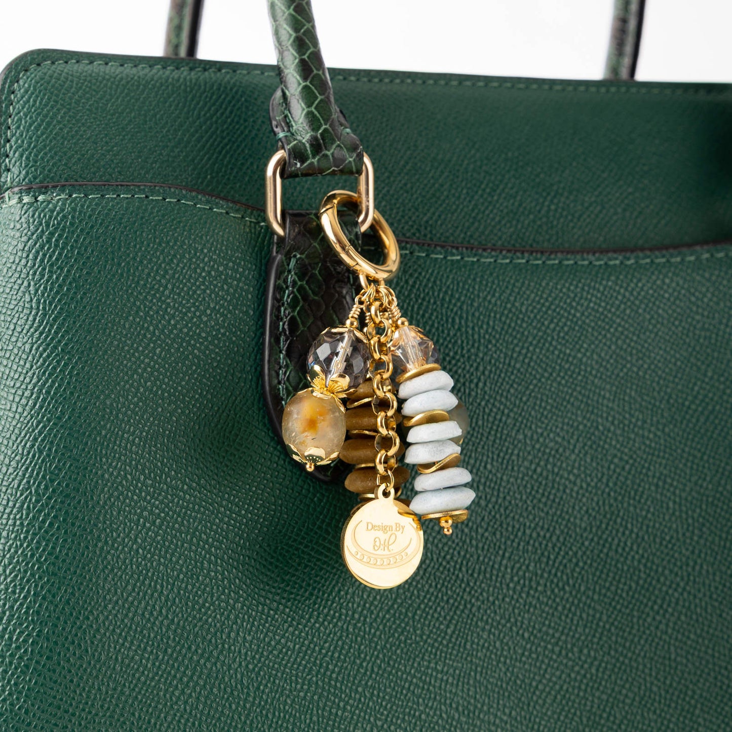 Close-up of Osaebea charm showing recycled glass beads in soft blue and warm brown with gold wavy disc accents.