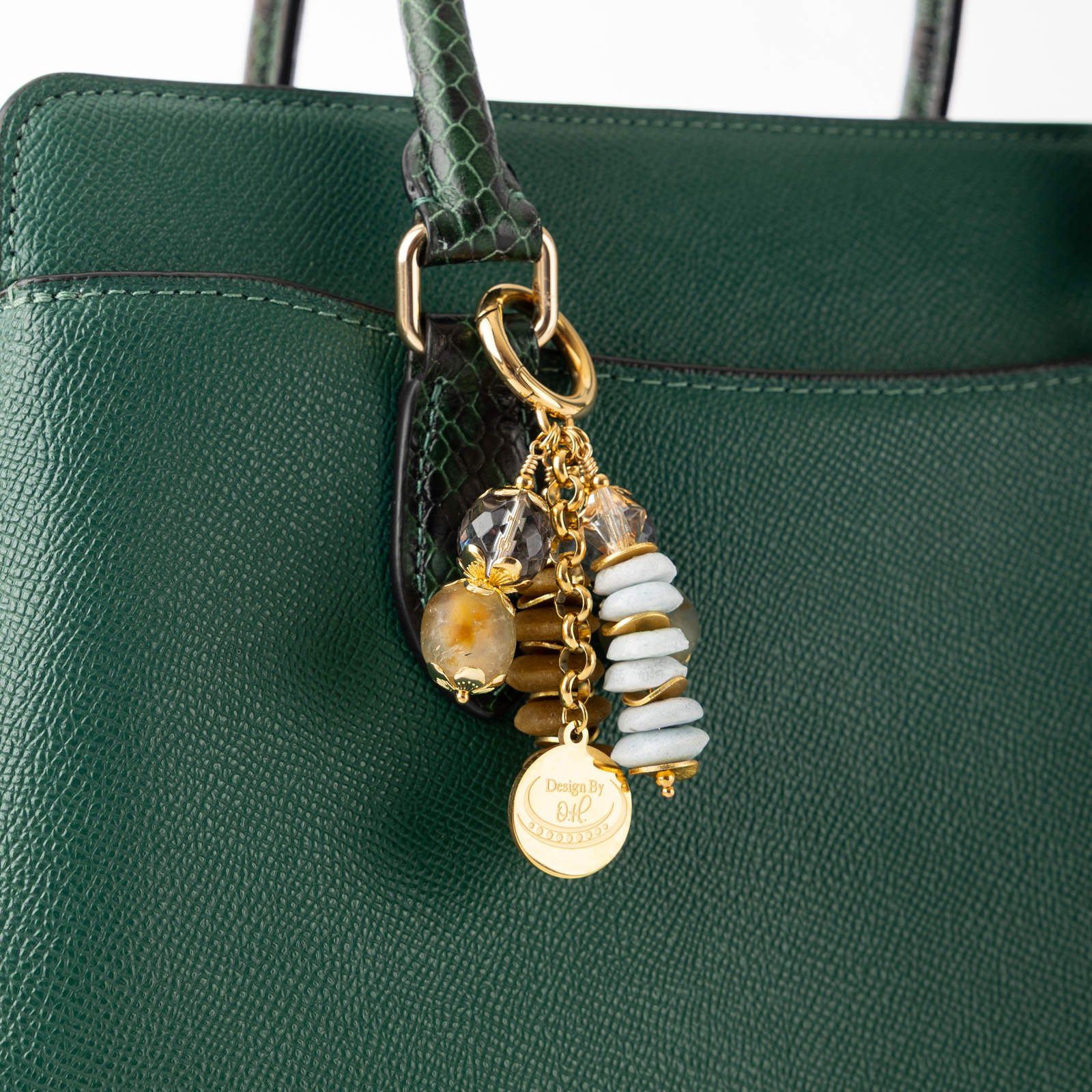 Close-up of Osaebea charm showing recycled glass beads in soft blue and warm brown with gold wavy disc accents.